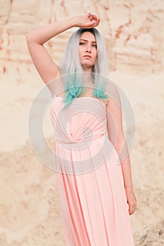 Young beautiful Caucasian woman in long pink dress posing in desert landscape with sand.