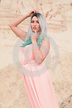 Young beautiful Caucasian woman in long pink dress posing in desert landscape with sand.