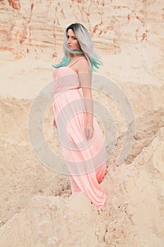 Young beautiful Caucasian woman in long pink dress posing in desert landscape with sand.