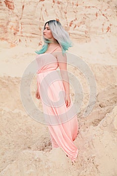 Young beautiful Caucasian woman in long pink dress posing in desert landscape with sand.