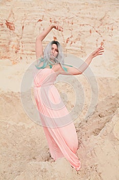 Young beautiful Caucasian woman in long pink dress posing in desert landscape with sand.