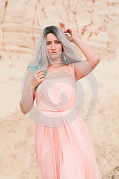 Young beautiful Caucasian woman in long pink dress posing in desert landscape with sand.