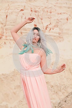 Young beautiful Caucasian woman in long pink dress posing in desert landscape with sand.