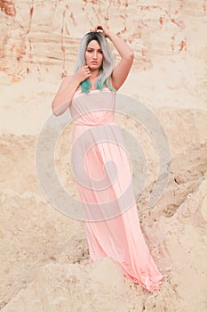 Young beautiful Caucasian woman in long pink dress posing in desert landscape with sand.