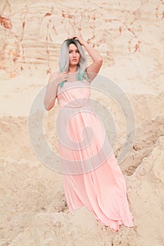 Young beautiful Caucasian woman in long pink dress posing in desert landscape with sand.