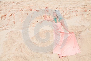 Young beautiful Caucasian woman in long pink dress posing in desert landscape with sand.