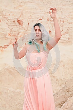 Young beautiful Caucasian woman in long pink dress posing in desert landscape with sand.