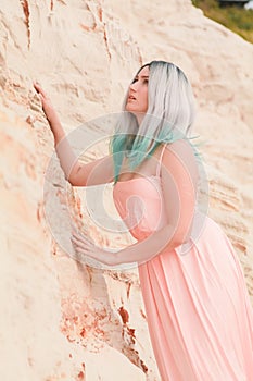 Young beautiful Caucasian woman in long pink dress posing in desert landscape with sand.