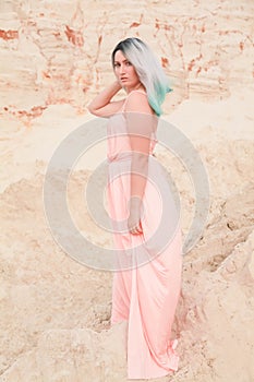 Young beautiful Caucasian woman in long pink dress posing in desert landscape with sand.