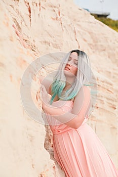 Young beautiful Caucasian woman in long pink dress posing in desert landscape with sand.