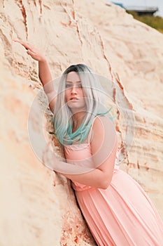 Young beautiful Caucasian woman in long pink dress posing in desert landscape with sand.