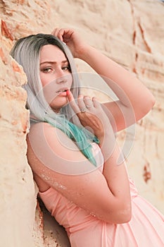 Young beautiful Caucasian woman in long pink dress posing in desert landscape with sand.