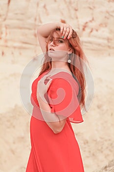 Young beautiful Caucasian woman in long red dress posing in desert landscape with sand.