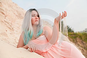 Young beautiful Caucasian woman posing in desert landscape with sand. Girl touch sand by palms.