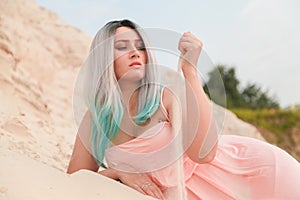 Young beautiful Caucasian woman posing in desert landscape with sand. Girl touch sand by palms.