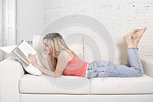 Young beautiful caucasian woman reading book studying lying comfortable on home sofa looking happy