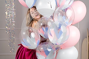 young beautiful caucasian woman in a red dress stands near balloons closed her eyes and enjoys the moment.