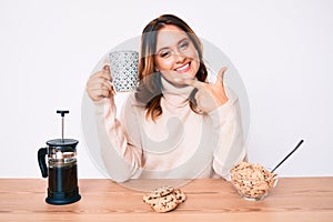 Young beautiful caucasian woman sitting on the table having breakfast smiling happy pointing with hand and finger