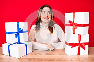 Young beautiful caucasian woman sitting on the table with presents looking to side, relax profile pose with natural face and