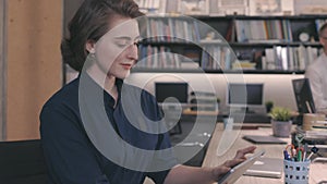 Young beautiful Caucasian woman using a digital tablet in office workspace while colleagues are working