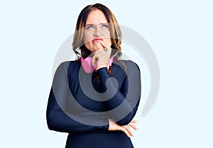 Young beautiful caucasian woman wearing gym clothes and using headphones serious face thinking about question with hand on chin,
