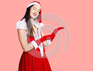 Young beautiful caucasian woman wearing santa claus costume inviting to enter smiling natural with open hand
