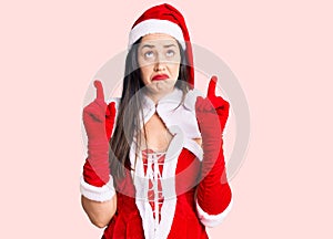 Young beautiful caucasian woman wearing santa claus costume pointing up looking sad and upset, indicating direction with fingers,