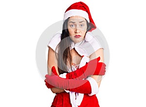 Young beautiful caucasian woman wearing santa claus costume shaking and freezing for winter cold with sad and shock expression on