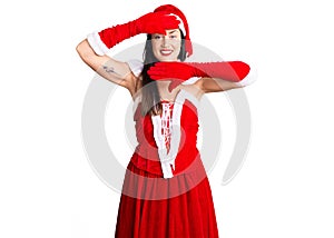Young beautiful caucasian woman wearing santa claus costume smiling cheerful playing peek a boo with hands showing face