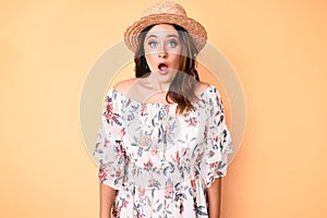 Young beautiful caucasian woman wearing summer dress and hat afraid and shocked with surprise expression, fear and excited face