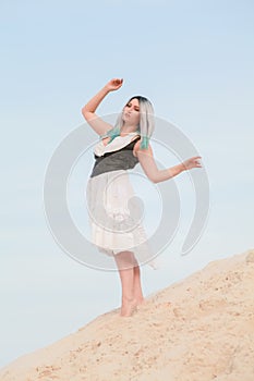 Young beautiful Caucasian woman in white dress and brown leather waistcoat posing in desert landscape with sand.