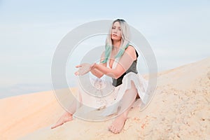 Young beautiful Caucasian woman in white dress and brown leather waistcoat posing in desert landscape with sand.