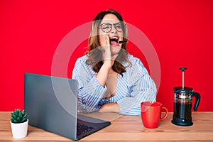 Young beautiful caucasian woman working at the office wearing operator headset shouting and screaming loud to side with hand on