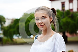 Young beautiful cheerful female student smiling, holding folders outdoors, park background.