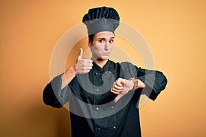 Young beautiful chef woman wearing cooker uniform and hat standing over yellow background Doing thumbs up and down, disagreement