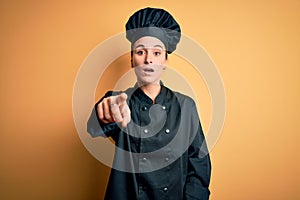 Young beautiful chef woman wearing cooker uniform and hat standing over yellow background pointing displeased and frustrated to