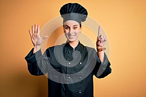 Young beautiful chef woman wearing cooker uniform and hat standing over yellow background showing and pointing up with fingers