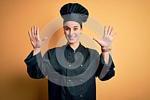 Young beautiful chef woman wearing cooker uniform and hat standing over yellow background showing and pointing up with fingers