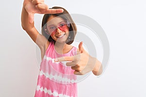 Young beautiful child girl wearing pink t-shirt and sunglasses over isolated white background smiling making frame with hands and