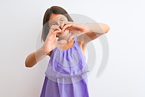 Young beautiful child girl wearing purple casual dress standing over isolated white background smiling in love showing heart