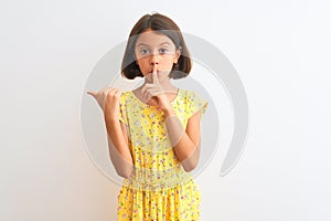 Young beautiful child girl wearing yellow floral dress standing over isolated white background asking to be quiet with finger on