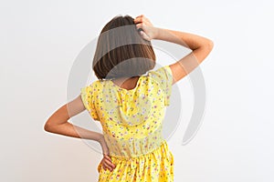 Young beautiful child girl wearing yellow floral dress standing over isolated white background Backwards thinking about doubt with