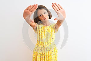 Young beautiful child girl wearing yellow floral dress standing over isolated white background doing frame using hands palms and