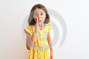 Young beautiful child girl wearing yellow floral dress standing over isolated white background hand on mouth telling secret rumor,