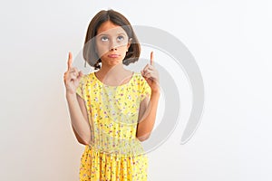 Young beautiful child girl wearing yellow floral dress standing over isolated white background Pointing up looking sad and upset,