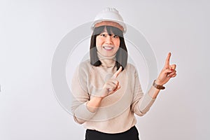 Young beautiful Chinese architect woman wearing helmet over isolated white background smiling and looking at the camera pointing