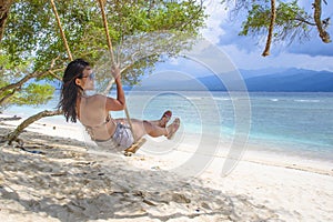 Young beautiful Chinese Asian girl having fun on beach tree swing enjoying happy feeling free in Summer holiday tropical trip