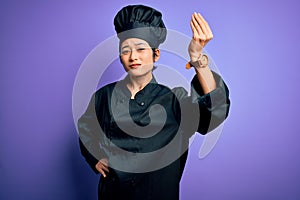 Young beautiful chinese chef woman wearing cooker uniform and hat over purple background Doing Italian gesture with hand and