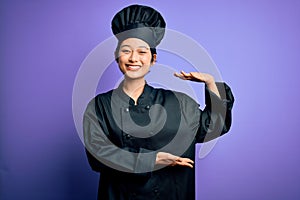 Young beautiful chinese chef woman wearing cooker uniform and hat over purple background gesturing with hands showing big and