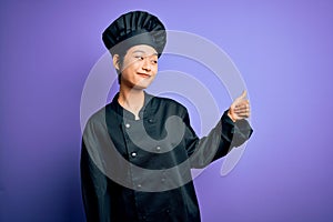 Young beautiful chinese chef woman wearing cooker uniform and hat over purple background Looking proud, smiling doing thumbs up